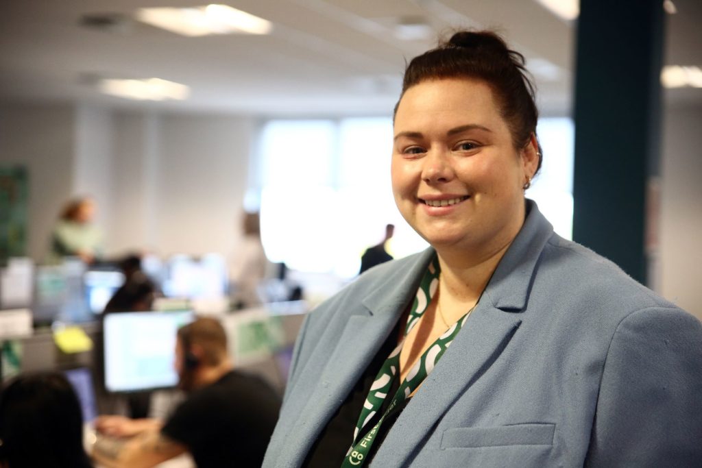 Gemma McGhee smiling side on with the AO Contact Centre blurred in the background